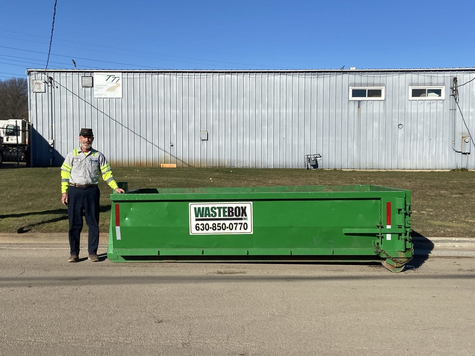 WasteBox driver Ken beside a green roll-off container outside the Lemont yard