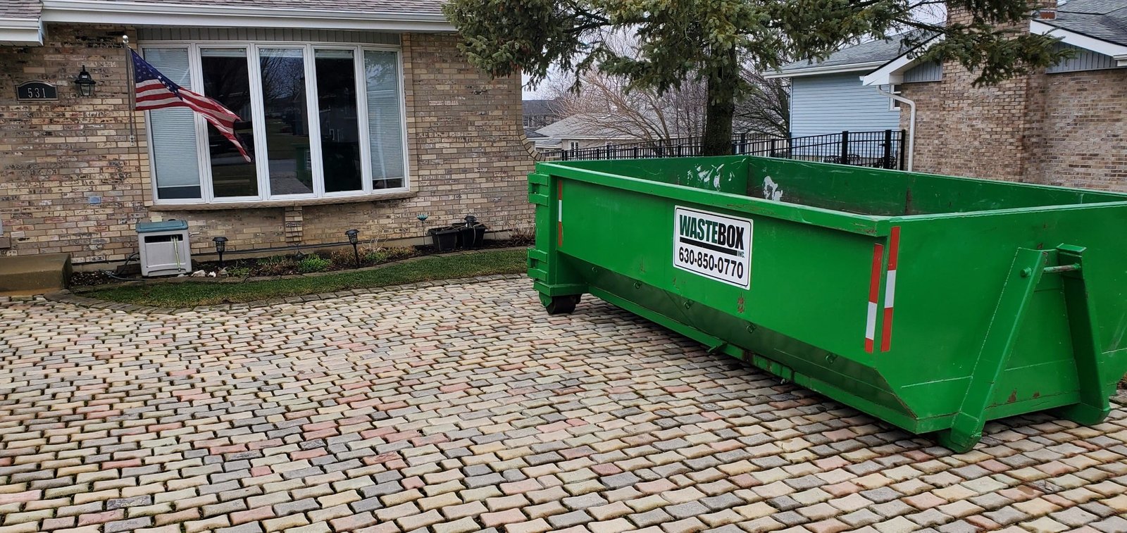 Green WasteBox dumpster placed on a paver driveway at a brick home