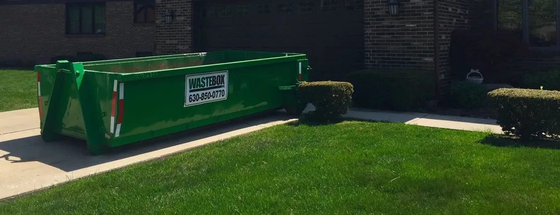 An empty green WasteBox roll-off container dropped beside a residential driveway